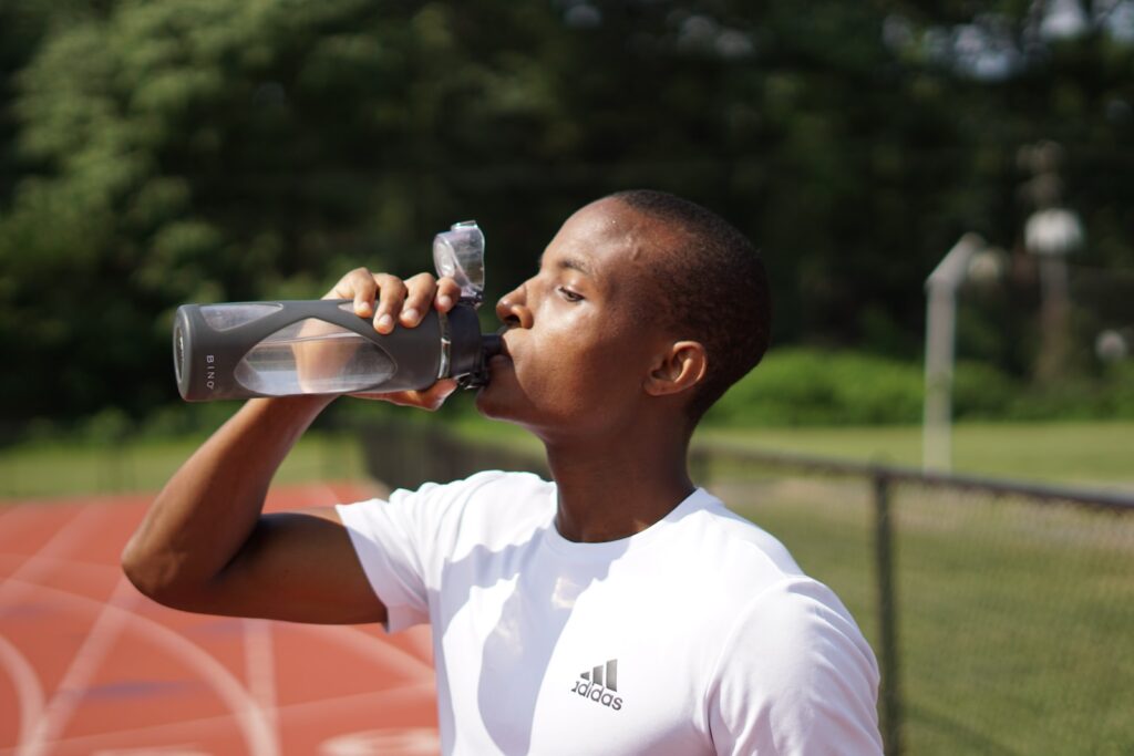 man in white crew neck t-shirt drinking from black sports bottle